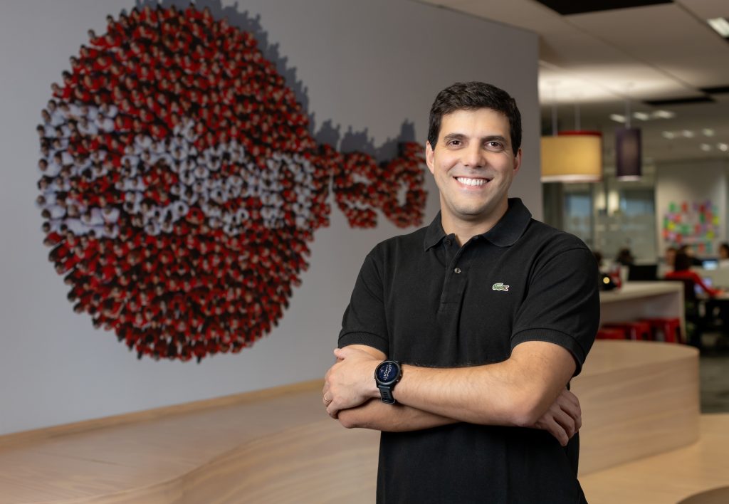 Executivo da Edenred Brasil posa em ambiente corporativo, com logotipo da empresa formado por fotos de pessoas ao fundo.