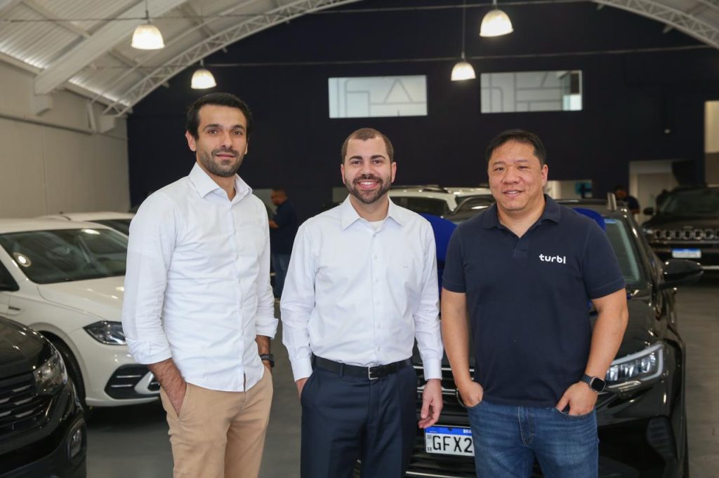 Executivos da Turbi em espaço de frota de veículos da empresa.