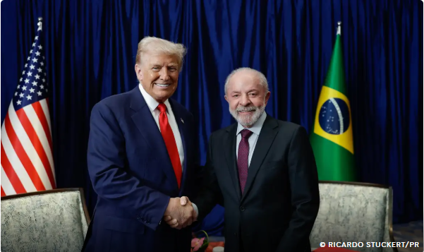 Donald Trump e Luiz Inácio Lula da Silva apertam as mãos em encontro oficial, com bandeiras dos Estados Unidos e do Brasil ao fundo.