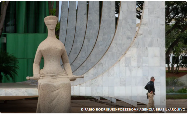 Estátua da Justiça em frente ao prédio do Supremo Tribunal Federal, com um agente caminhando ao fundo.