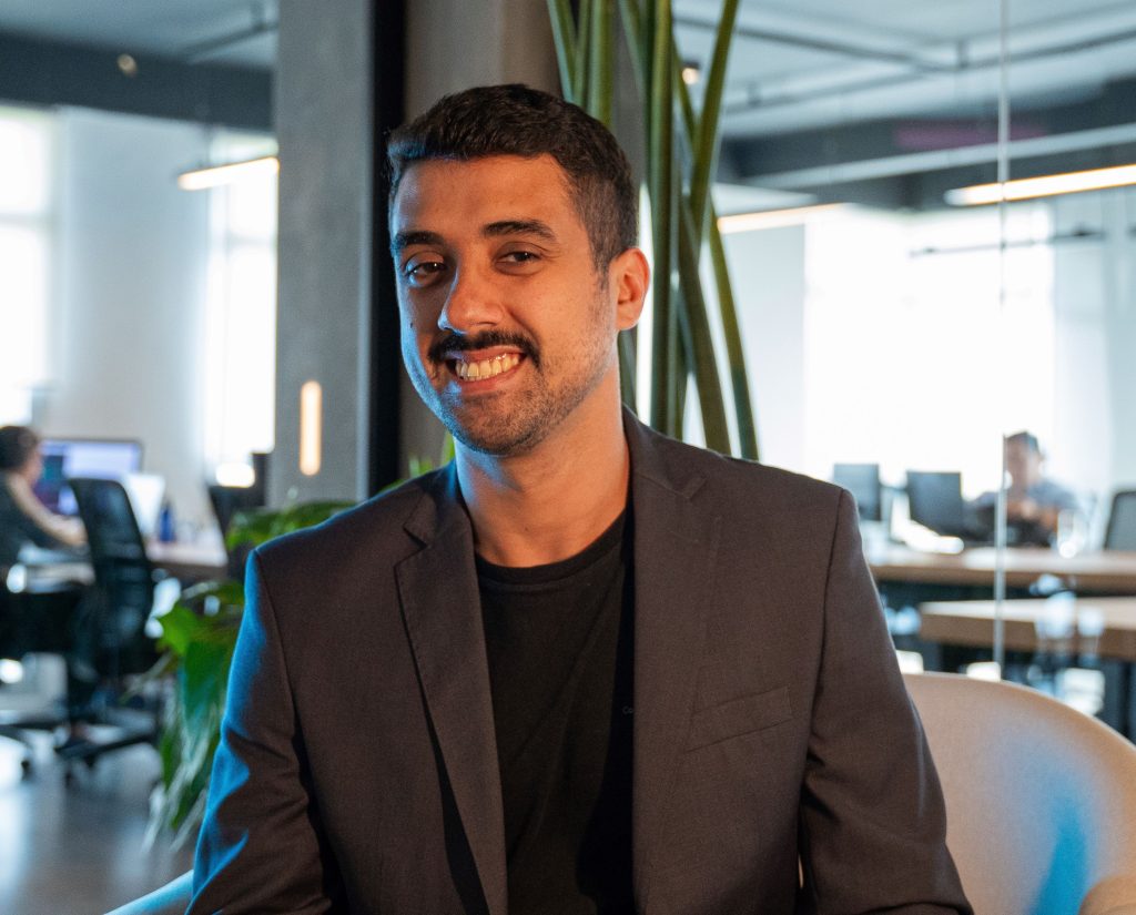 Retrato de Joab Júnior, especialista em qualidade de software, sentado em escritório moderno, sorrindo.
