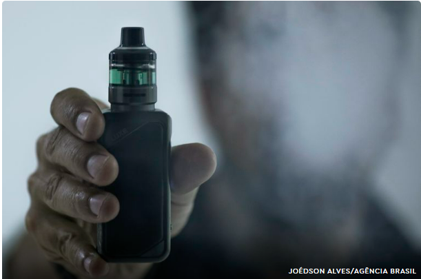 Homem segura cigarro eletrônico enquanto solta vapor, em referência ao uso de vapes no Brasil