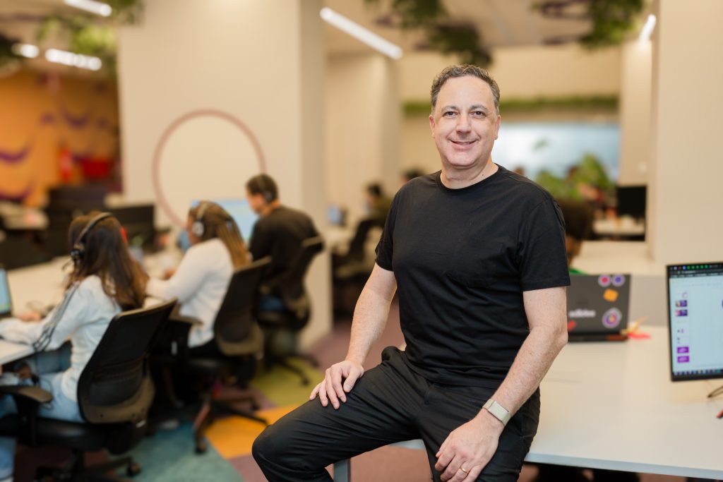 Ale Garcia, co-CEO e cofundador da Sólides, em ambiente corporativo com equipe ao fundo.