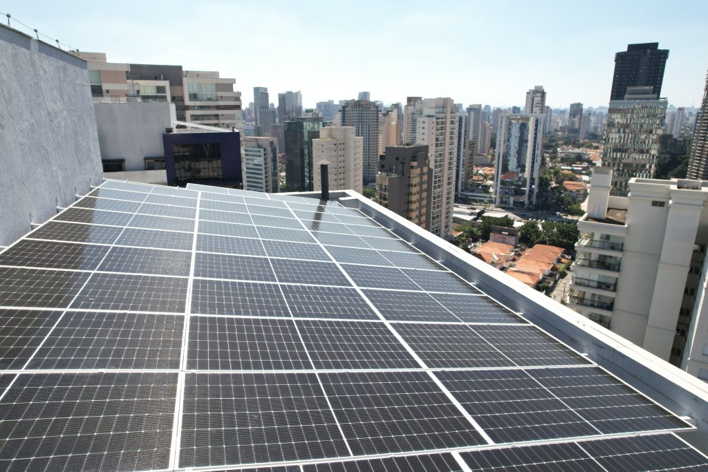 Painéis solares fotovoltaicos instalados na cobertura de um edifício, com skyline de São Paulo ao fundo.