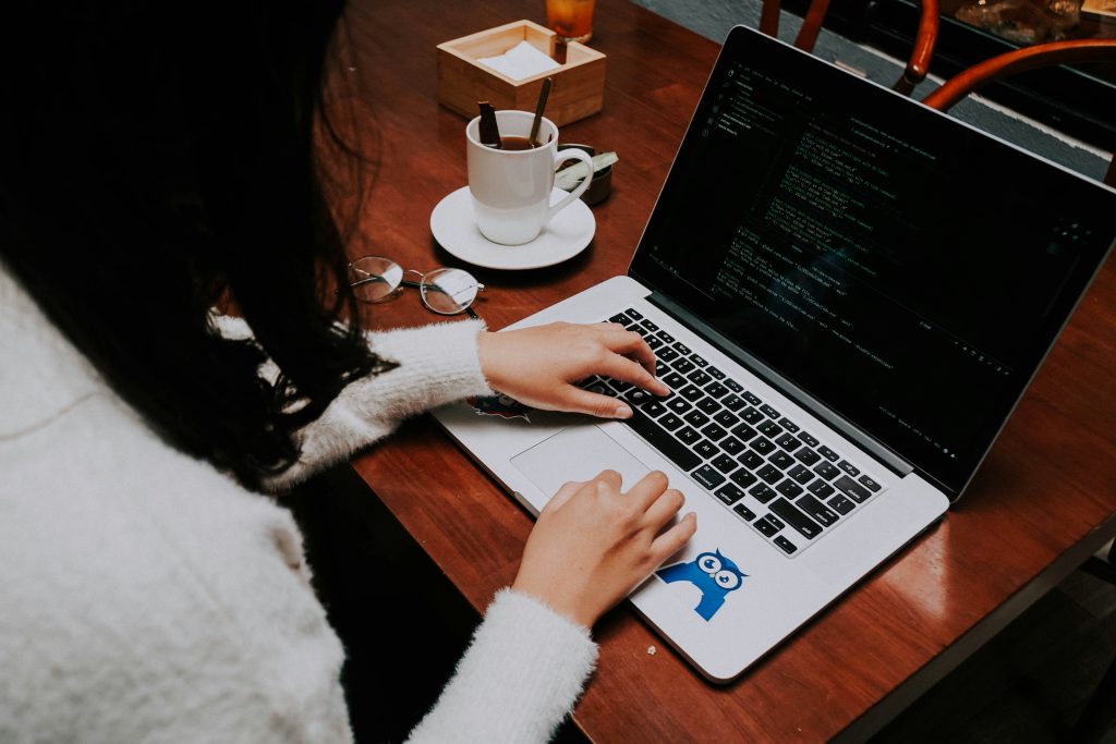 Mãos digitando em notebook com tela de código, xícara de café ao lado.